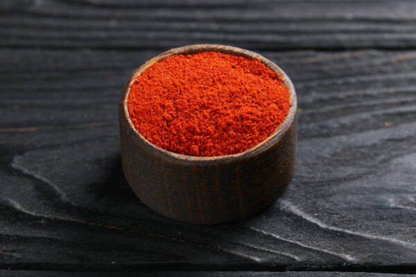 Ground paprika spice in a wooden saucepan on black wooden table