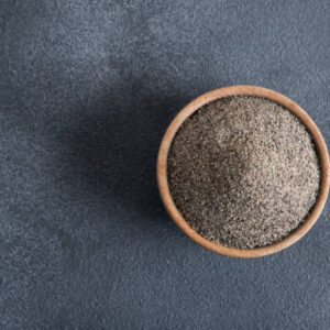 Bowl full of black peppercorns on black background