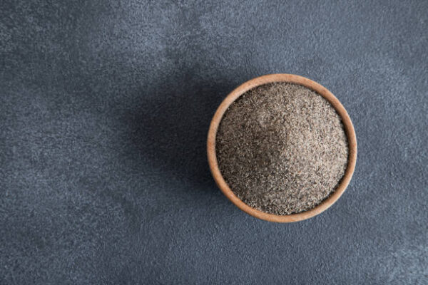 Bowl full of black peppercorns on black background